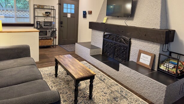 Un salon doté d’une cheminée, d’un téléviseur à écran plat fixé au-dessus, d’un canapé, d’une table basse et d’un coin cuisine équipé d’un four à micro-ondes et d’un grille-pain.
