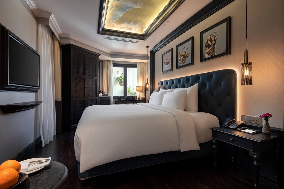 Una habitación de hotel elegante con una cama grande, un escritorio con teléfono y bloc de notas, un televisor montado en la pared y obras de arte enmarcadas.