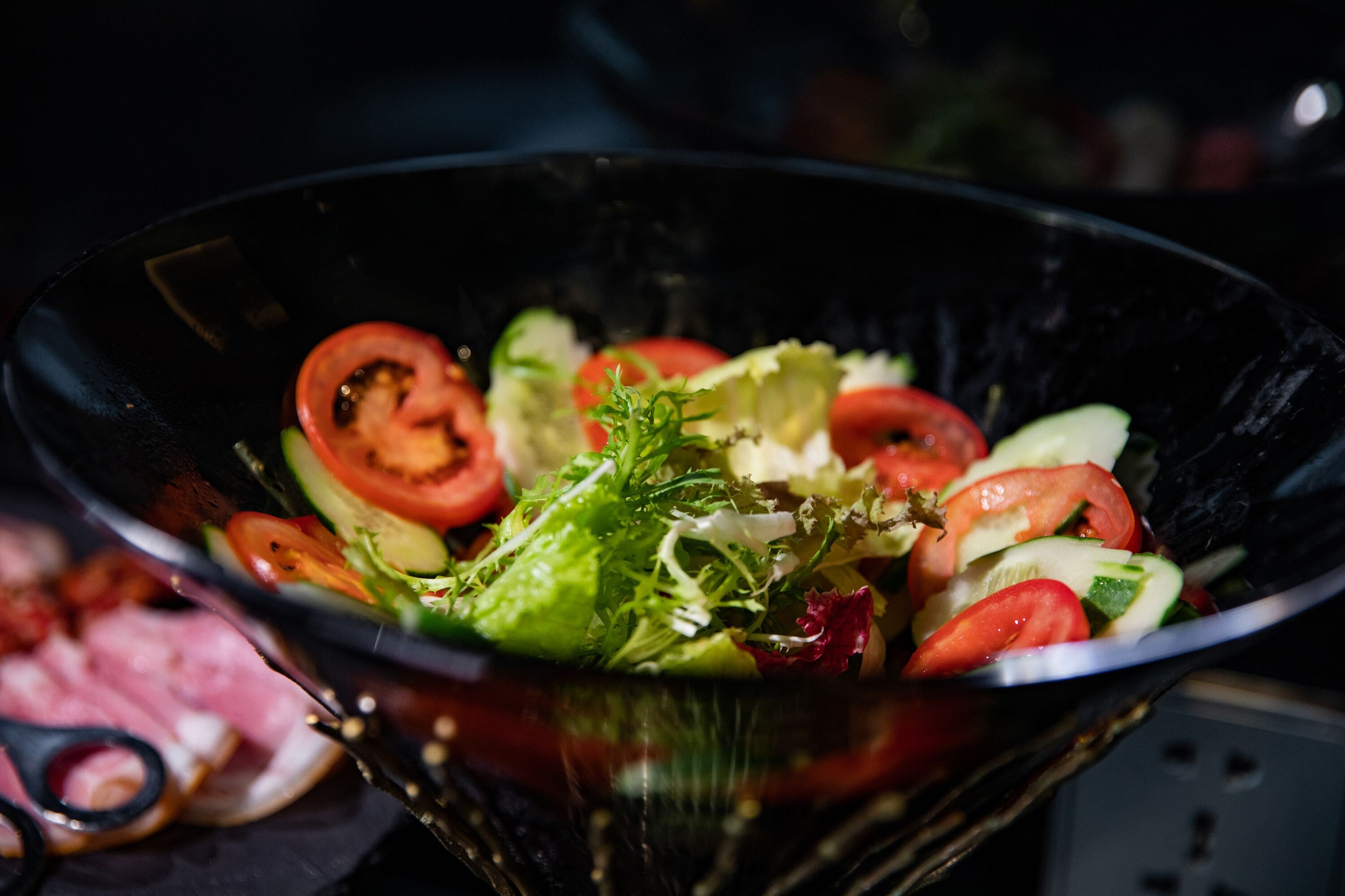 A salad in a black bowl with visible ingredients like lettuce, tomatoes, and cucumbers.