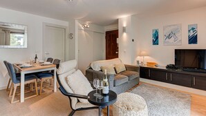 A modern living room with a dining area, a sofa set, a TV, and artwork on the walls. - Apartment Cosmiques - Alpes Agency - Central Chamonix - Sleeps 4 (Chamonix-Mont-Blanc)