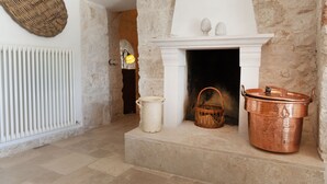 A stone-walled room with a fireplace, a white radiator, a woven basket, and a copper pot. - Trullo of Mariluna in Valle d'Itria (Selva di Fasano)