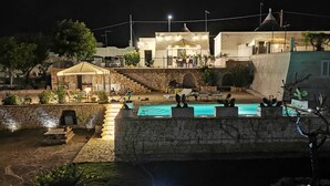 A nighttime view of a villa with a swimming pool, outdoor seating, and a stone wall. - Trullo of Mariluna in Valle d'Itria (Selva di Fasano)