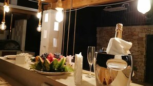 A wooden interior with hanging light bulbs, a fruit platter, a bottle of champagne, and a rustic fireplace. - Trullo of Mariluna in Valle d'Itria (Selva di Fasano)