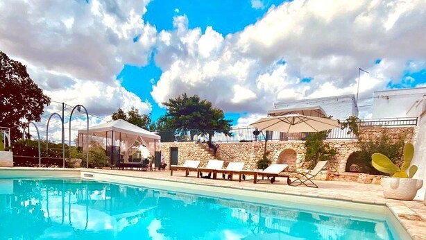 A pool area with lounge chairs and a covered seating area, surrounded by stone walls and a clear blue sky. - Trullo of Mariluna in Valle d'Itria (Selva di Fasano)