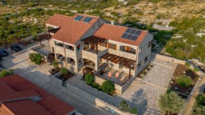 A two-story stone house with a red-tiled roof, solar panels, and a stone courtyard with seating. - Villa Shanti | Pool, Beach & Basketball court (Rt Veslo)
