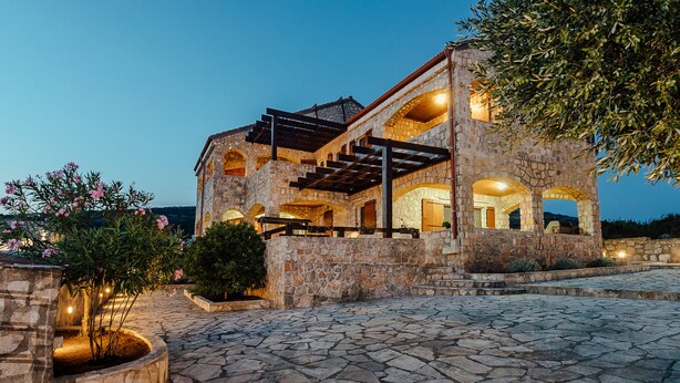 A stone building with arched windows and a covered patio area. - Villa Shanti | Pool, Beach & Basketball court (Rt Veslo)