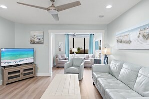 A living room with a television, a ceiling fan, a sofa, a chair, and a window with curtains. - "Salty Sun" - Golf Cart (included), Tennis, Pools, Golf, Beach... it's all here! (Destin)