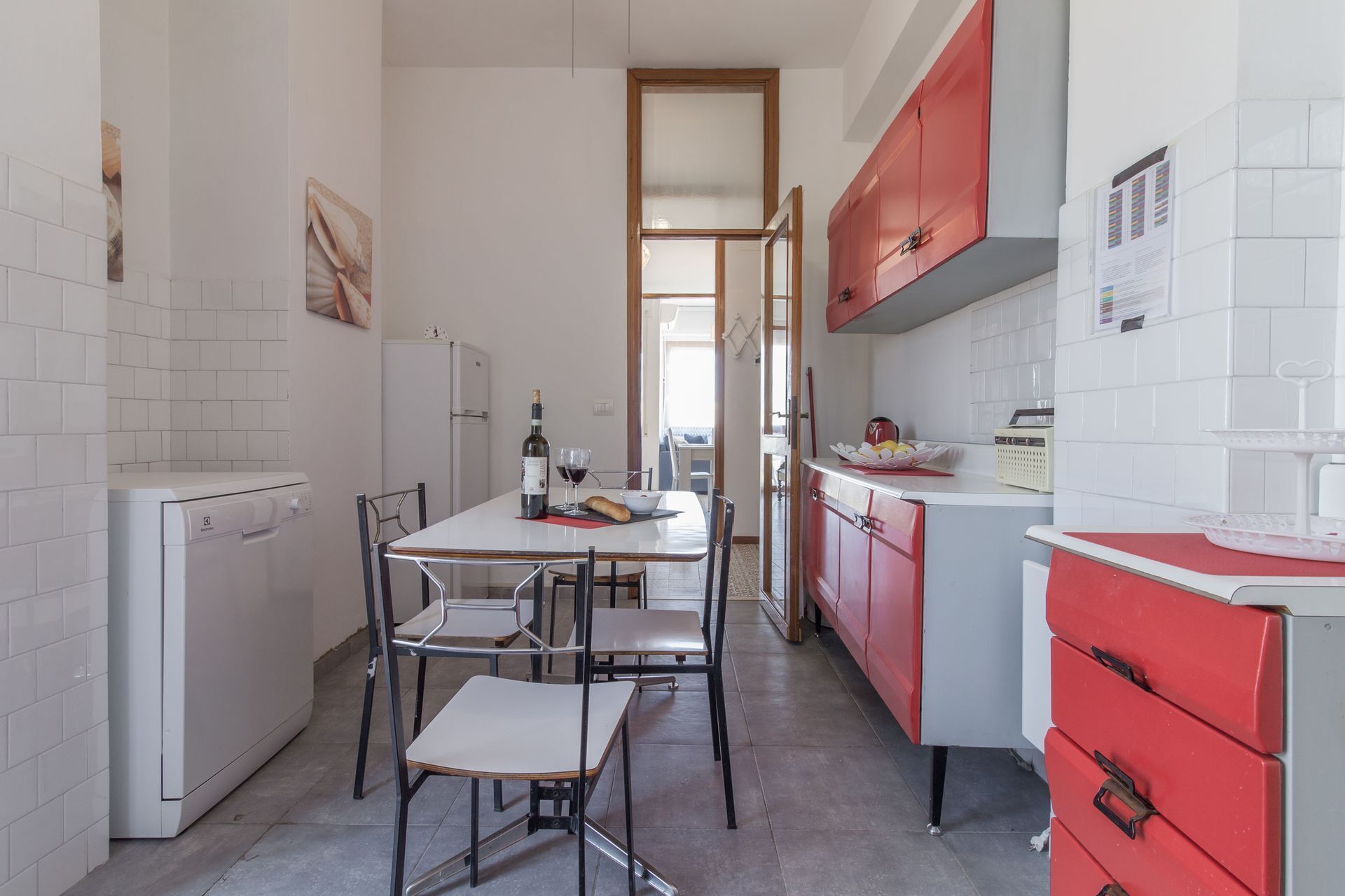 A compact kitchen with white and red cabinets, a dining table with chairs, and a refrigerator.