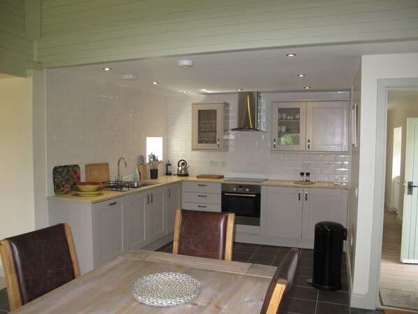Una cocina moderna con armarios blancos, una campana extractora de acero inoxidable y un comedor con mesa y sillas de madera.
