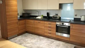 A modern kitchen with wooden cabinets, a stainless steel Bosch oven, a microwave, and a toaster. - Toothbrush Apartments - Ipswich Waterfront - Regatta Quay (Ipswich)