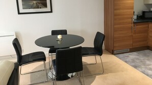 A small, modern kitchen with a round dining table and four chairs, a wooden cabinet, and a framed picture on the wall. - Toothbrush Apartments - Ipswich Waterfront - Regatta Quay (Ipswich)
