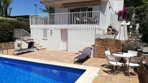 Zona junto a la piscina con una piscina azul cristalina, paredes blancas y un balcón con mobiliario exterior.