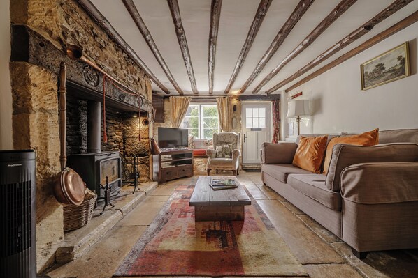 A traditional room with a stone fireplace, a television, a sofa, and a patterned rug. - COTSWOLD HISTORIC COTTAGE, WITH LARGE GARDEN (Naunton)