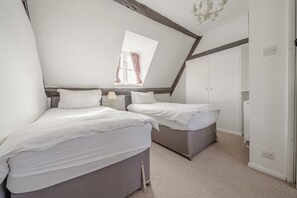 A bedroom with two beds, a window with curtains, a chandelier, and a white wardrobe. - COTSWOLD HISTORIC COTTAGE, WITH LARGE GARDEN (Naunton)