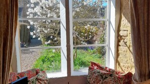 A room with a window seat, curtains, and a view of a garden. - COTSWOLD HISTORIC COTTAGE, WITH LARGE GARDEN (Naunton)