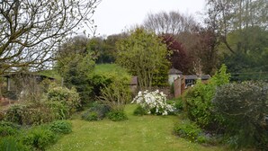 A garden with a variety of plants and a small building in the background. - COTSWOLD HISTORIC COTTAGE, WITH LARGE GARDEN (Naunton)