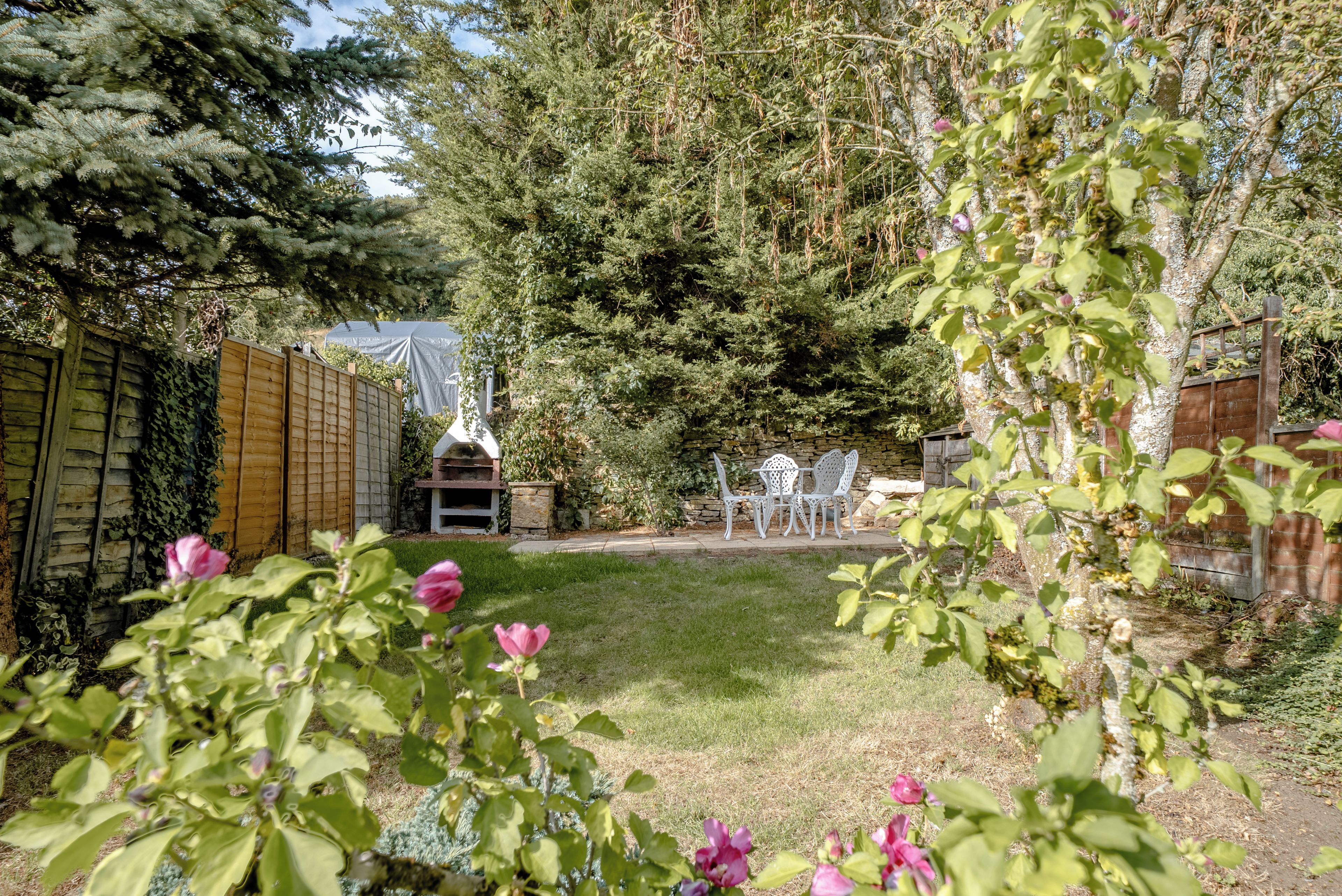 A garden with a stone wall, a wooden fence, and a barbecue area.