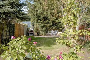 Ein Garten mit einer Steinsäule, einem Holzzaun und einem Grillplatz.