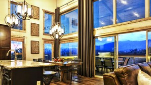 A spacious kitchen with a large island, dining area with chairs, and large windows offering a view of the outdoors.