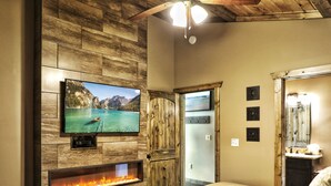 A room with a fireplace, a television mounted on a wooden wall, and a door leading to another room.