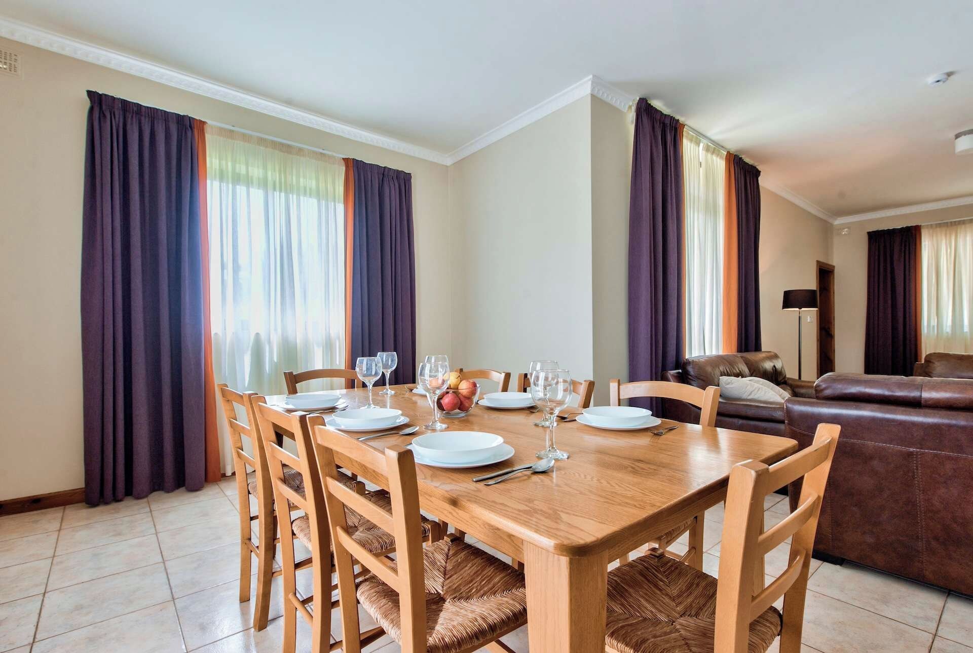 Un coin repas avec une table en bois, dressée pour quatre personnes, entourée de chaises dont les assises sont en osier tressé.