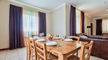 Un coin repas avec une table en bois, dressée pour quatre personnes, entourée de chaises dont les assises sont en osier tressé.
