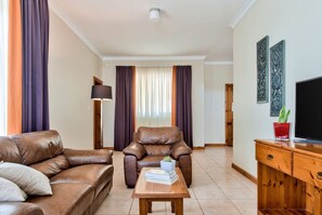 Una sala de estar con un sofá de cuero marrón, una mesa de centro de madera y un sillón marrón. Hay un televisor sobre un mueble de madera y una planta en la mesa.