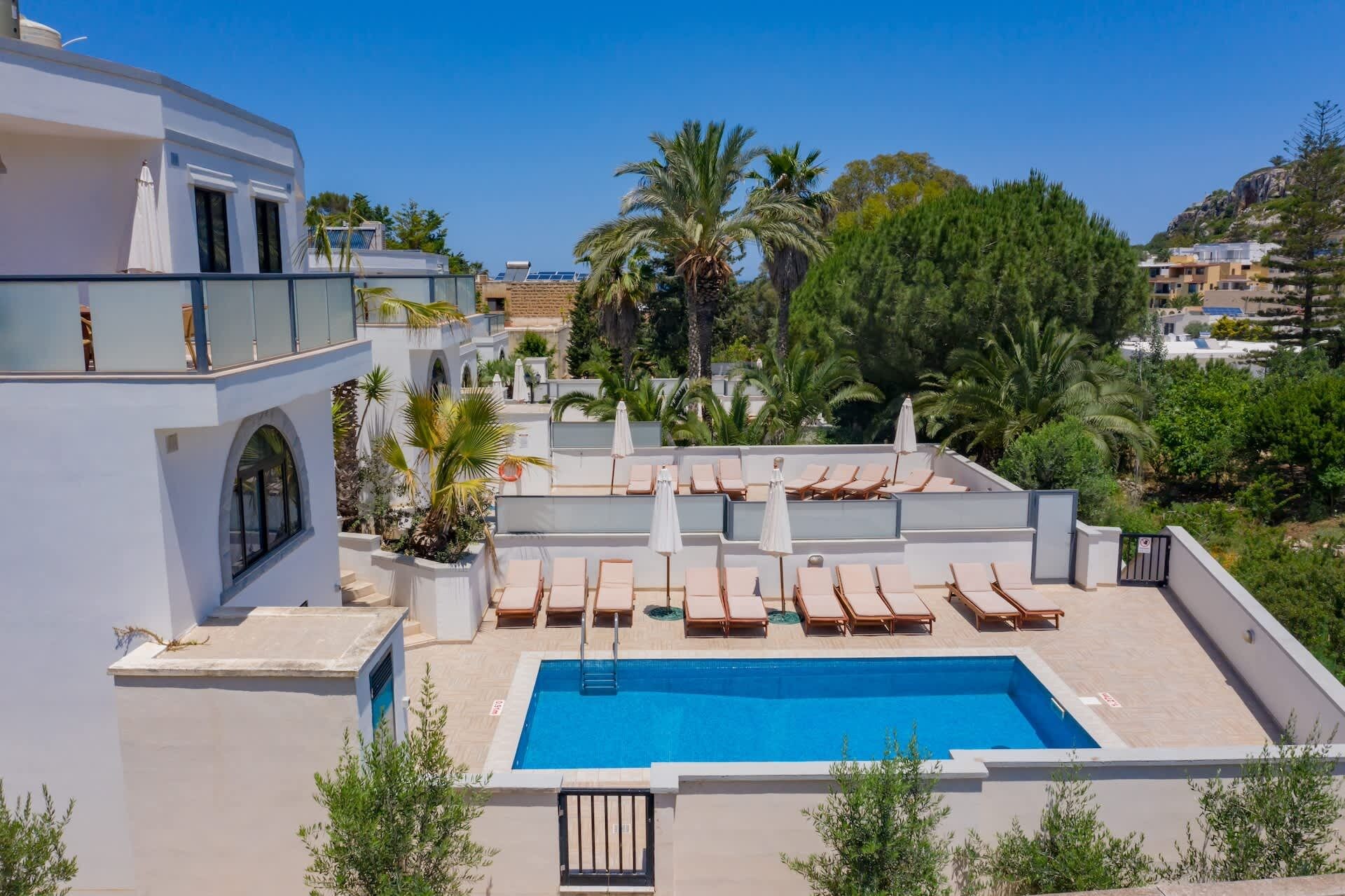 Area piscina sul tetto con poltrone relax e vasca, circondata da vegetazione e edifici.