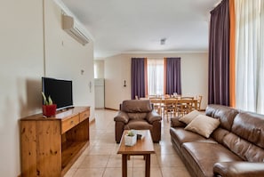 Una sala de estar con televisor, muebles de madera, un sofá de cuero y un comedor con mesa y sillas.