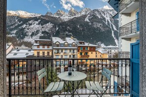 A balcony with a table and chairs, overlooking a mountain village with snow-covered buildings and a clear sky. - Apartment Kitson - Alpes Agency - Central Chamonix - Sleeps 6 (Chamonix-Mont-Blanc)