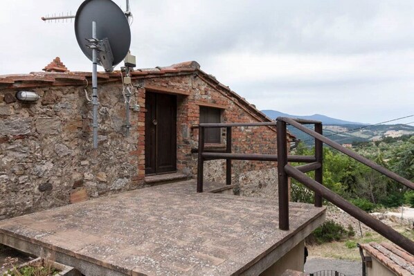 Un edificio rústico de piedra con una antena parabólica, una escalera de madera y vistas al campo.