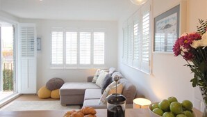 Una sala de estar con un sofá gris, una mesa de centro con croissants, un florero con flores y un cuenco de manzanas verdes.