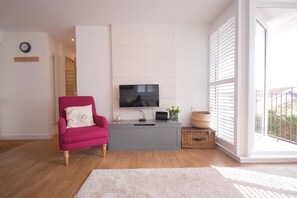 A living room with a pink armchair, a grey entertainment unit with a TV, a white rug, and a view through large windows. - Jack's Stay, stylish apartment, Salcombe, parking (Salcombe)