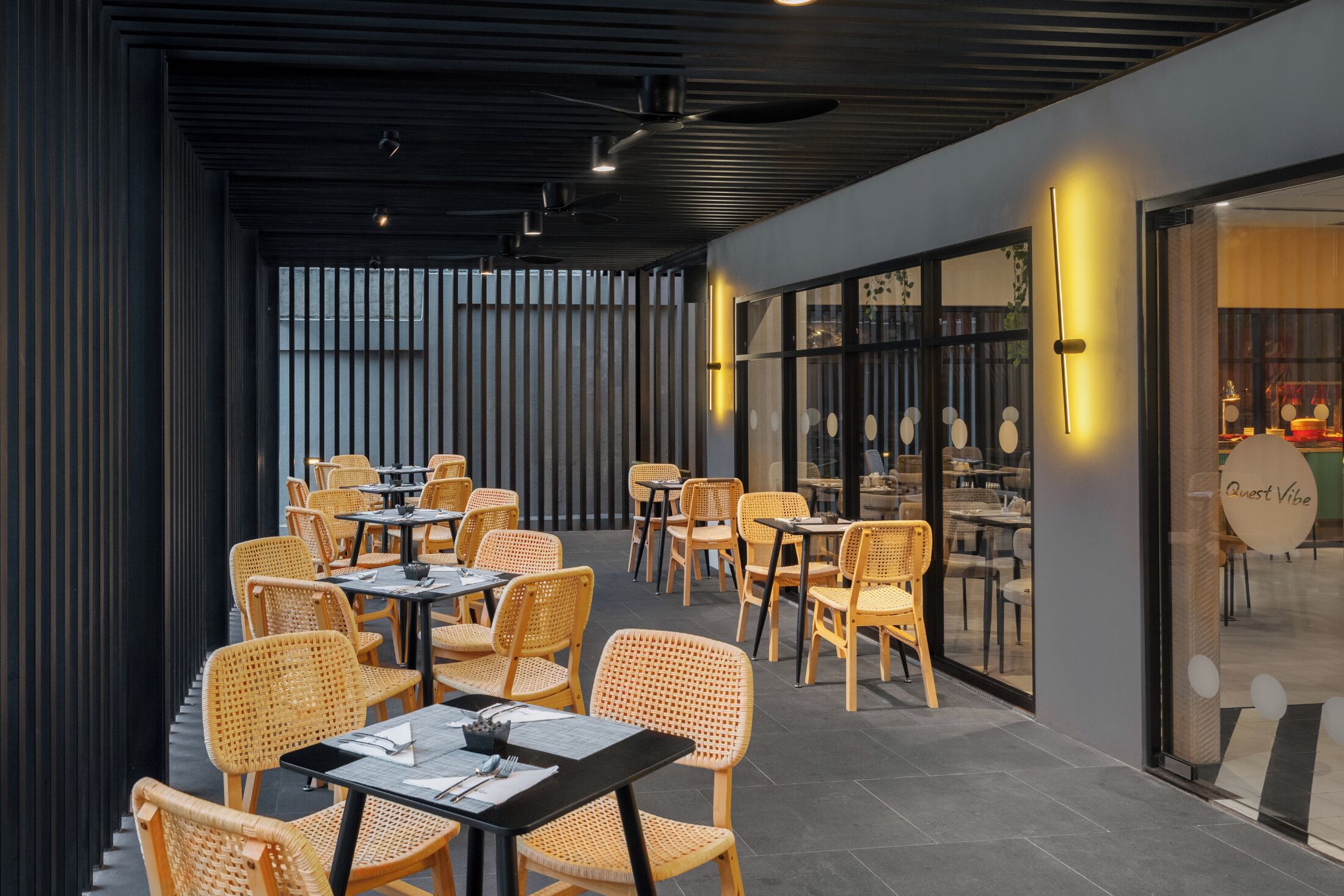 Een overdeelde eetruimte met rieten stoelen en tafels, een modern plafond en uitzicht op het restaurant door glazen deuren.
