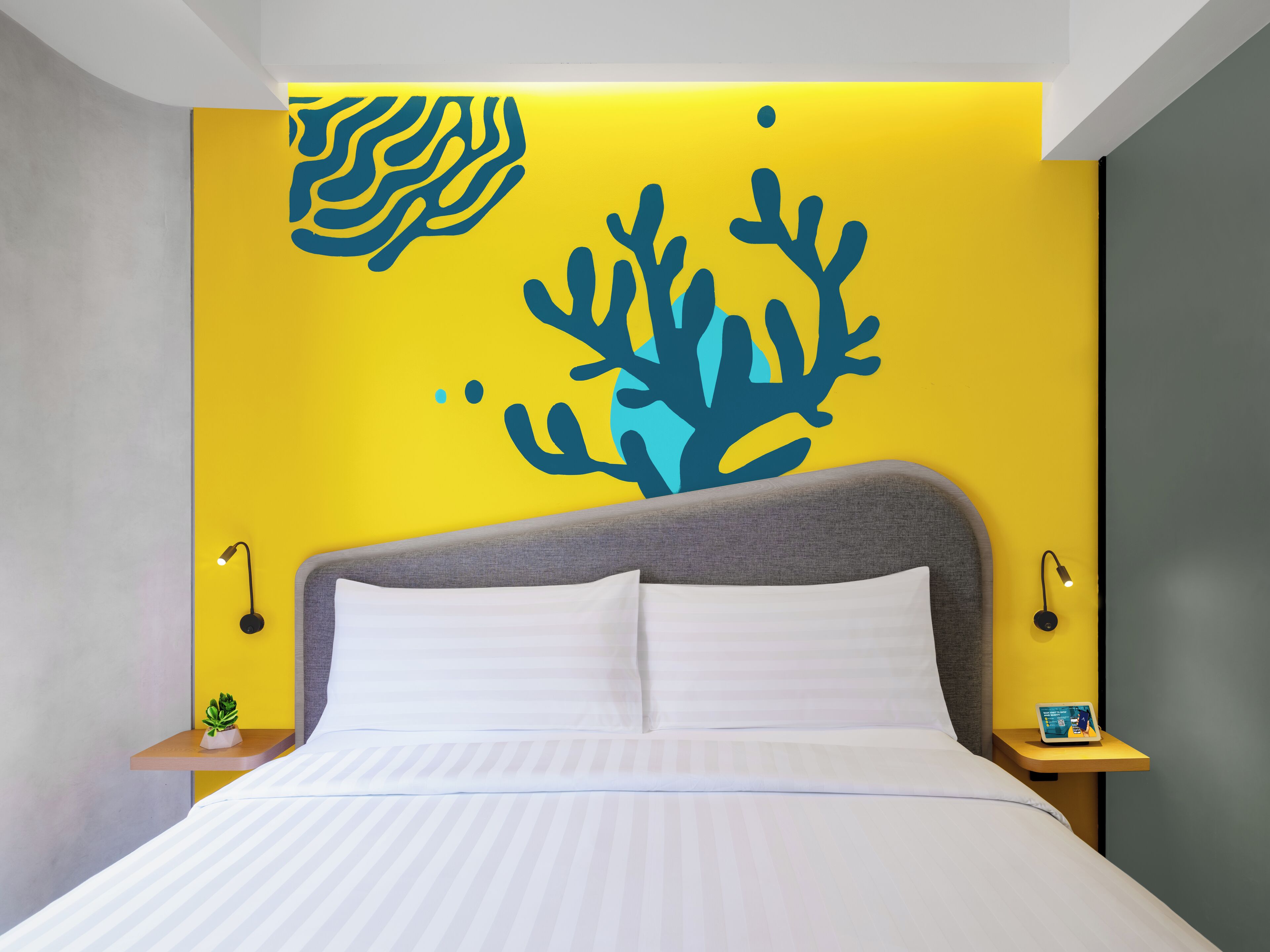 A modern bedroom with a bed, nightstands, and a wall with a coral reef mural.