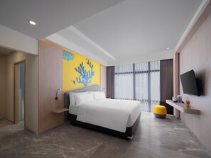A modern hotel room with a bed, a television, a large window with curtains, and a yellow accent wall. - Quest Vibe Dewi Sri Bali (Legian)