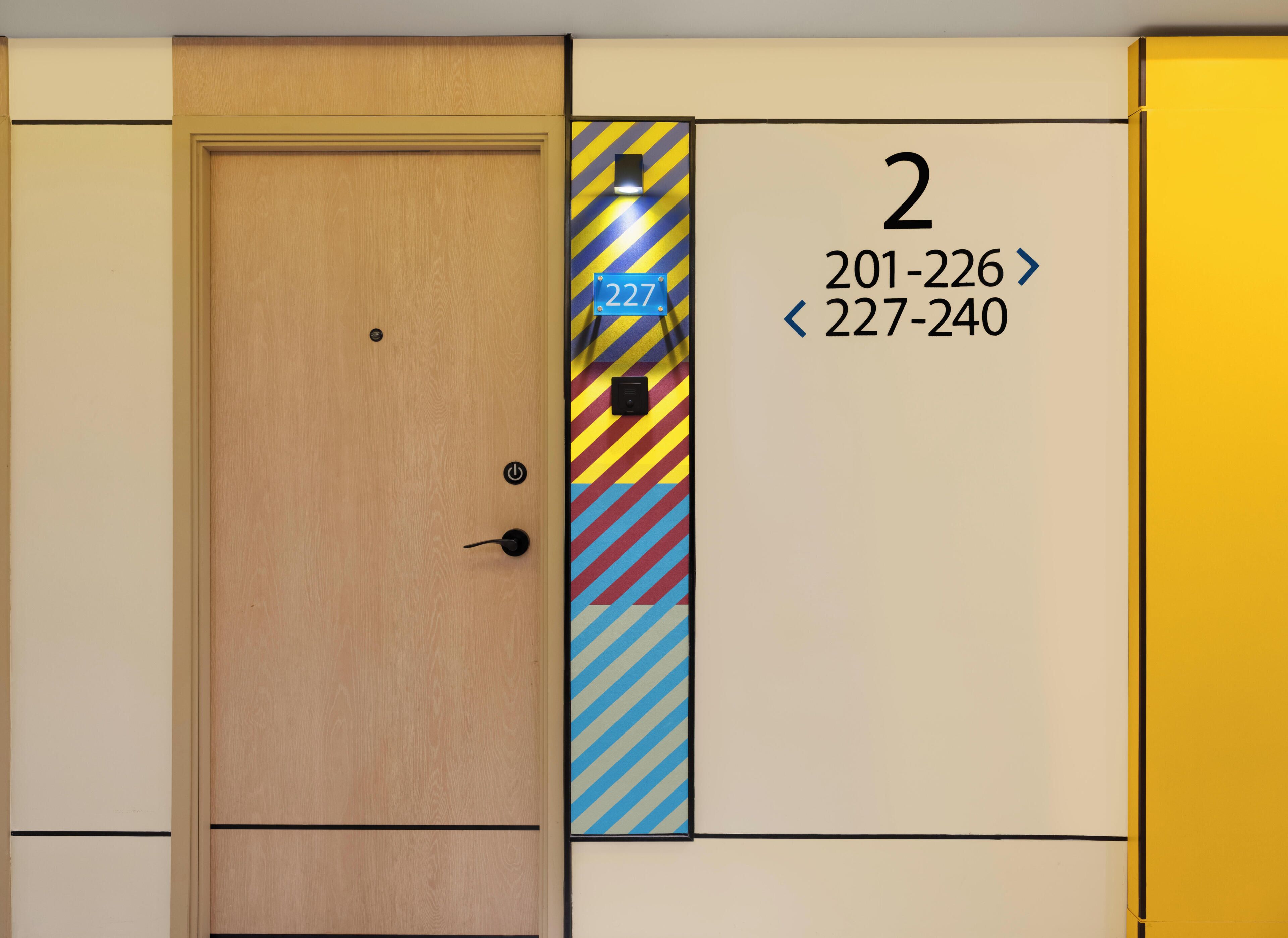 A hotel room with a wooden door, a number sign '2', and a color-coded panel with phone numbers.