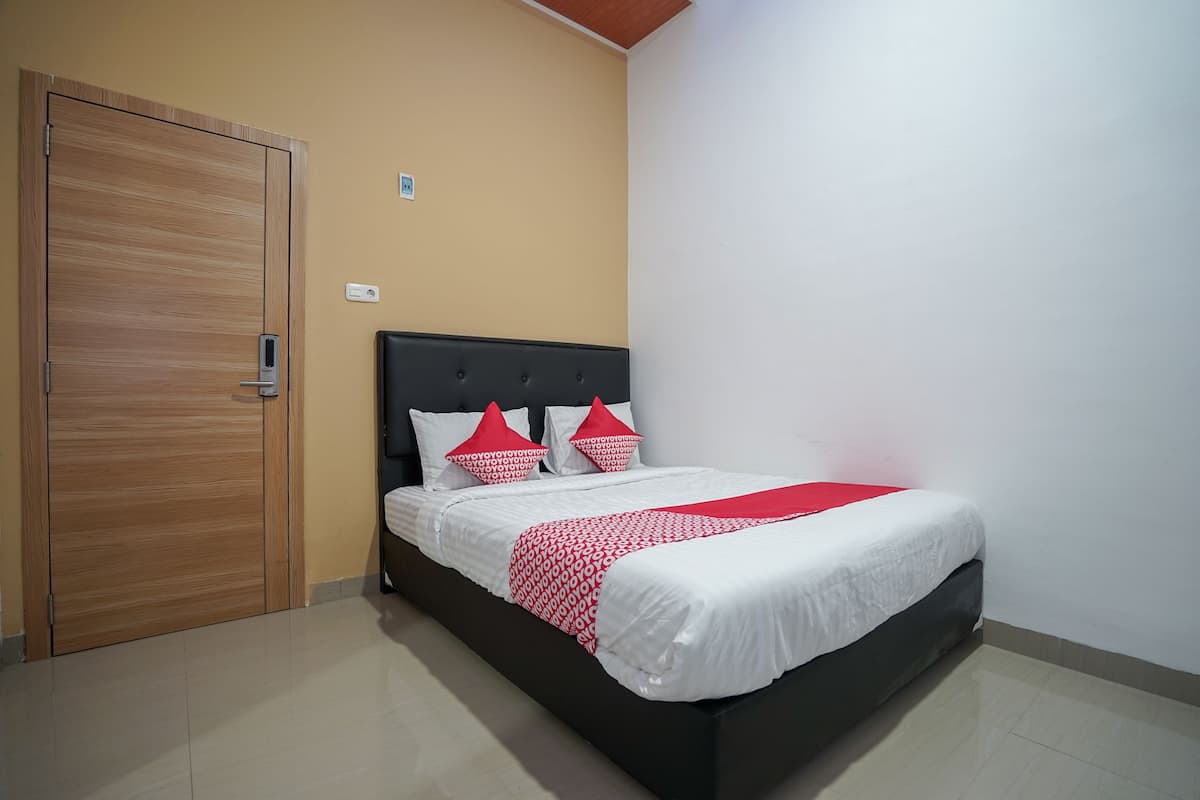 A bedroom with a wooden wardrobe, a bed with a black headboard, and a red and white patterned bedspread.