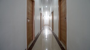 A long, narrow hallway with wooden doors on both sides and a shiny tiled floor. - OYO 945 Mega Kost 2 (Palembang)