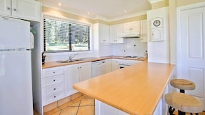 A kitchen with white cabinets, a wooden countertop, a built-in oven, and a window with blinds.