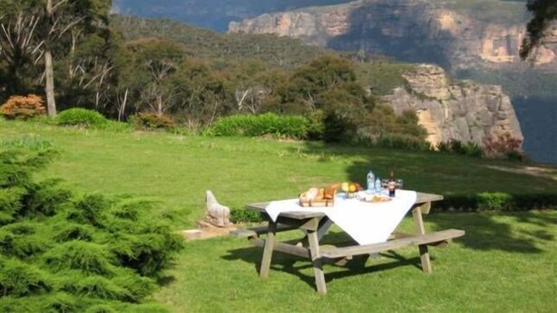 A picnic table set up on a grassy hill with a scenic view of cliffs and mountains in the background.