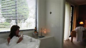 A woman in a bathtub with a bottle of champagne and candles.