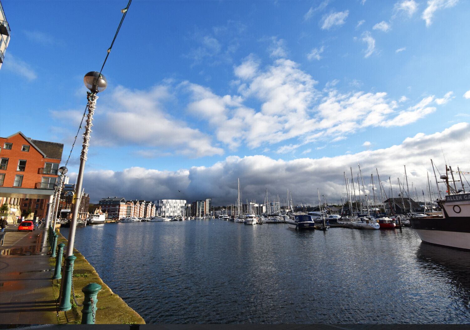 Un puerto deportivo con barcos amarrados, cielo despejado y edificios al fondo.