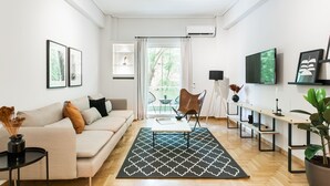A modern living room with a sofa, a coffee table, a patterned rug, a TV, and a potted plant. - Bright 2BD Apartment in Psychiko (Neo Psichiko)