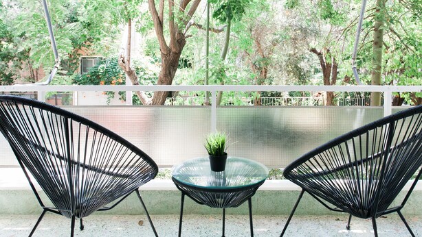 A balcony with two black wire mesh chairs and a small glass table with a potted plant. - Bright 2BD Apartment in Psychiko (Neo Psichiko)