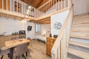 Une pièce confortable, de style rustique, aménagée comme un chalet, avec une table à manger en bois, un lit, une petite kitchenette et un escalier.