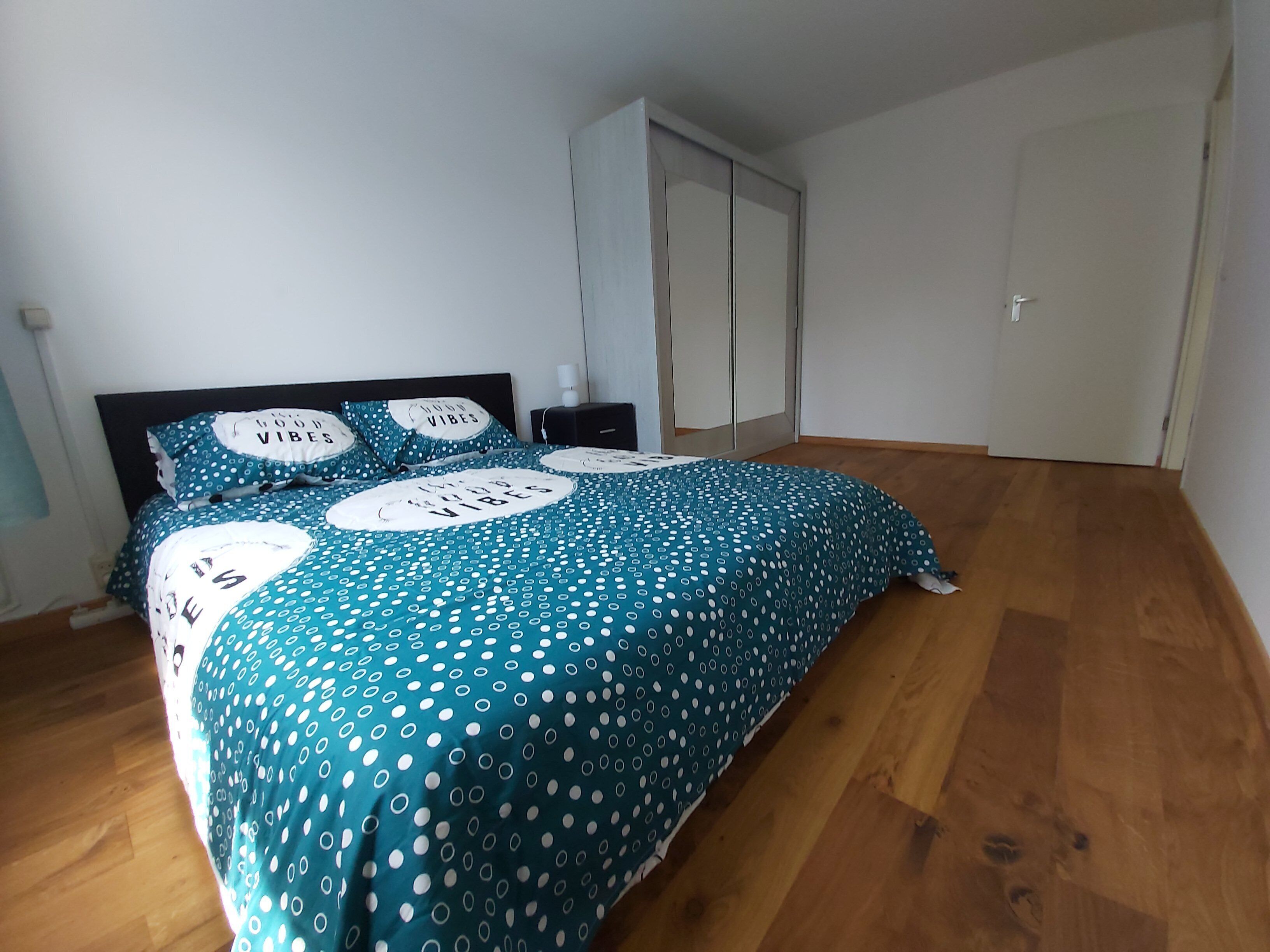 A bedroom with a bed, a nightstand, a wardrobe, and a door.