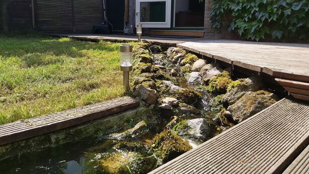 Ein Garten mit einem kleinen Teich, einer Holzterrasse und einer Steinmauer.