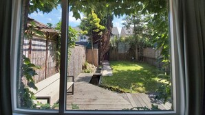 Blick durch ein Fenster auf einen Hinterhof mit einer Holzterrasse, einem Bambuszaun und einer Rasenfläche.