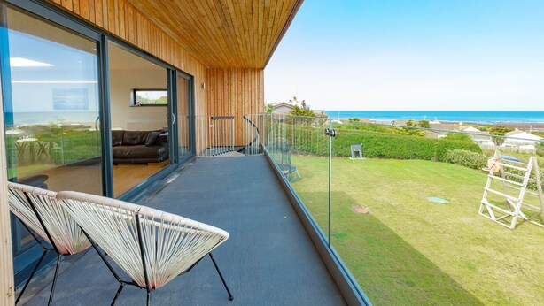 Un balcón con vista al mar, una puerta de cristal que da a un cuarto con sofá y una silla.